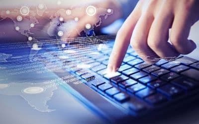 Hand typing on a laptop keyboard over a digital world map